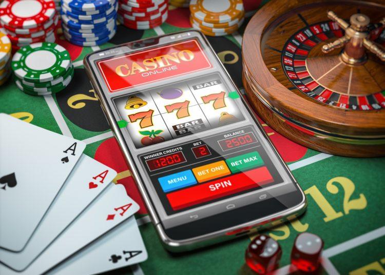 Casino online. Smartphone or mobile phone, slot machine, dice, cards and roulette on a green table in casino. 3d illustration